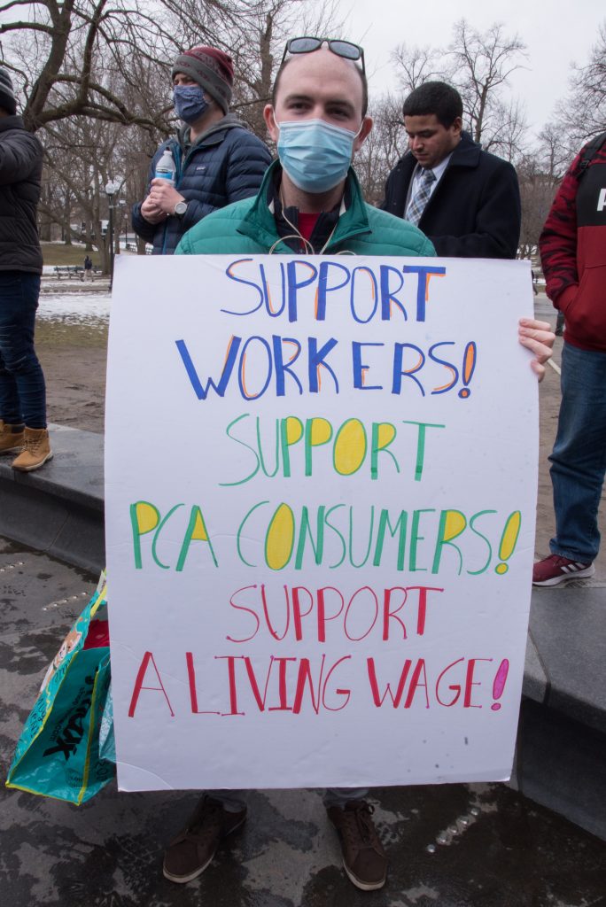 man with sign: SUpport Workers! Support PCA Consumers! Support a Living Wage!